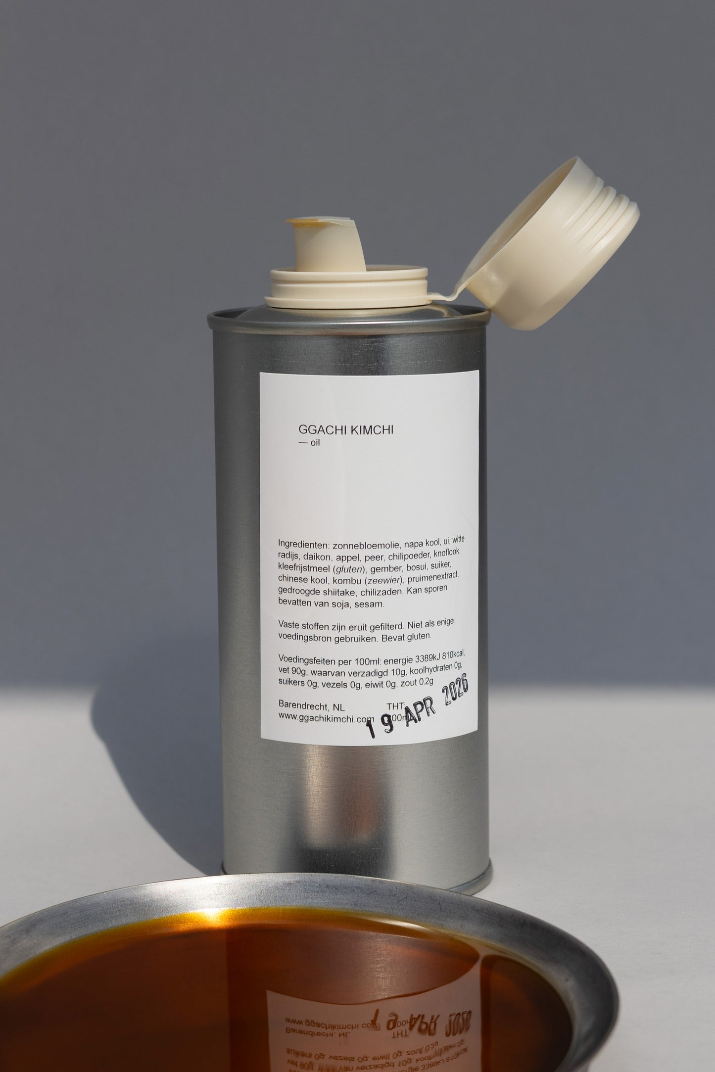 Metal canister with a white label on a gray background containing ggachi kimchi oil