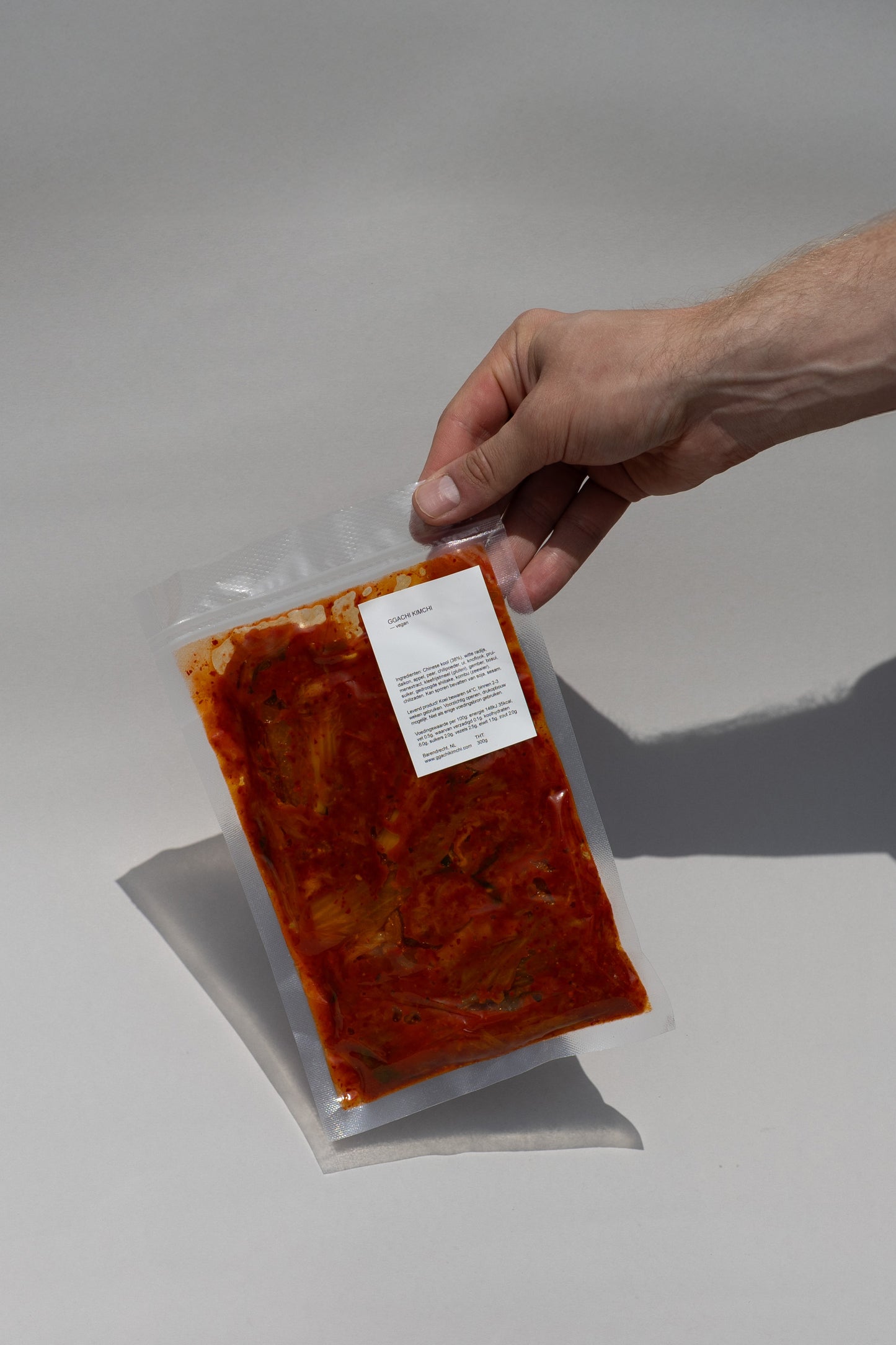 Hand holding a package of vegan kimchi with a label on a white background