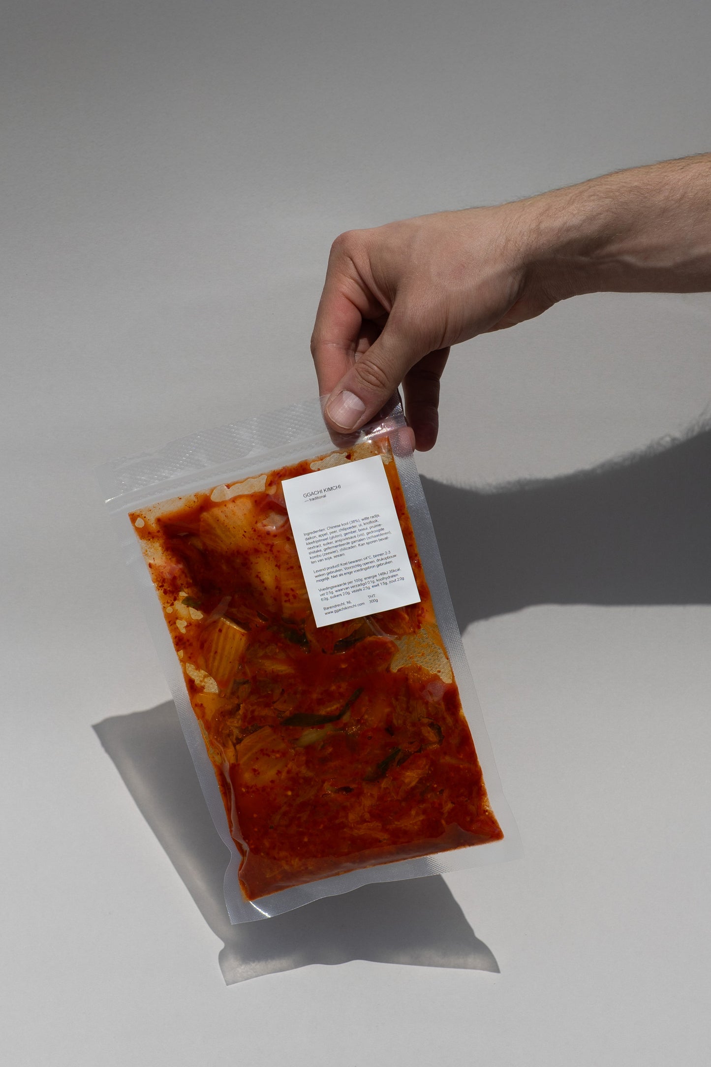 Hand holding a package of traditionl kimchi against a neutral background